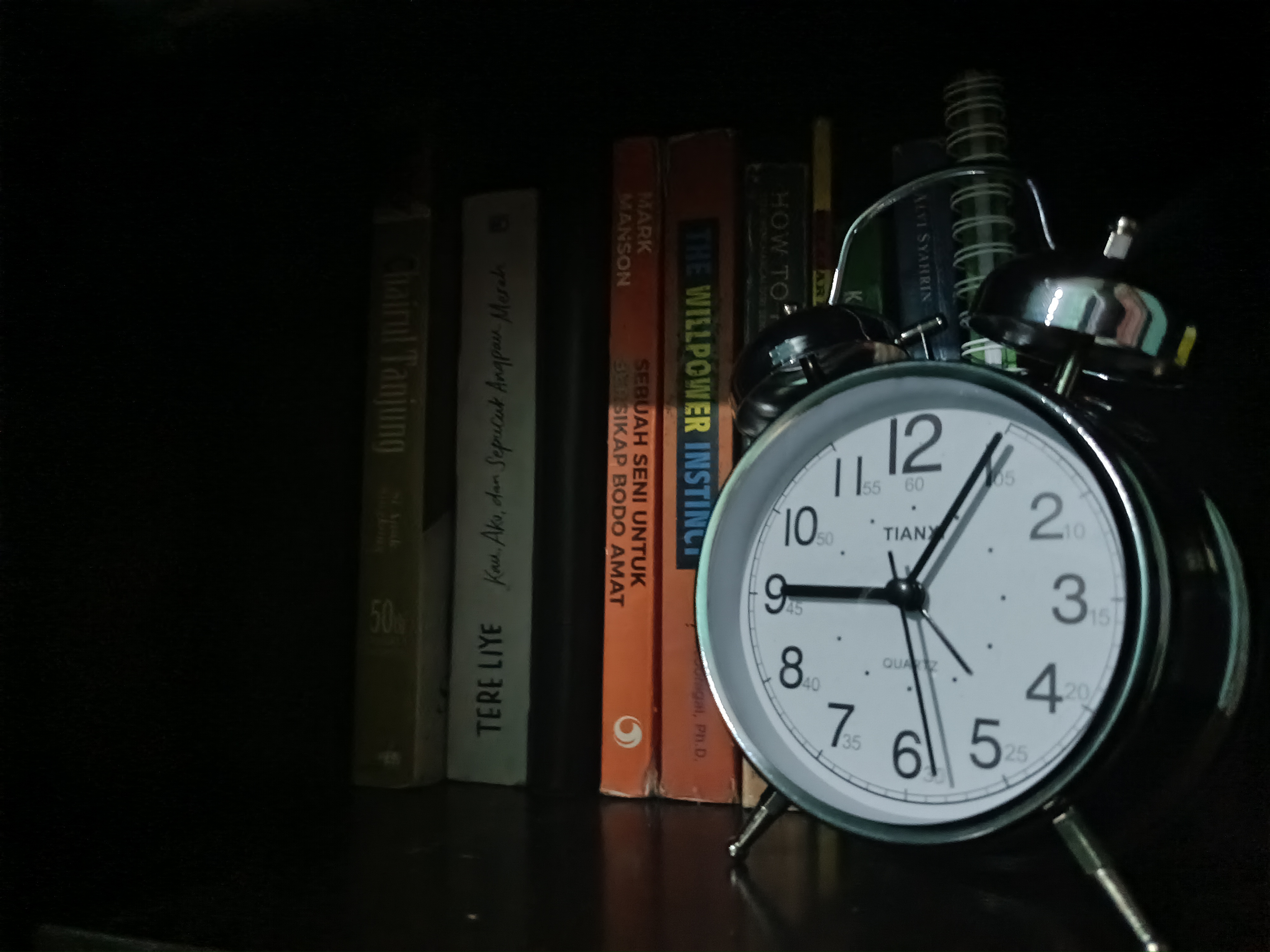 An alarm clock in front of books on a shelf