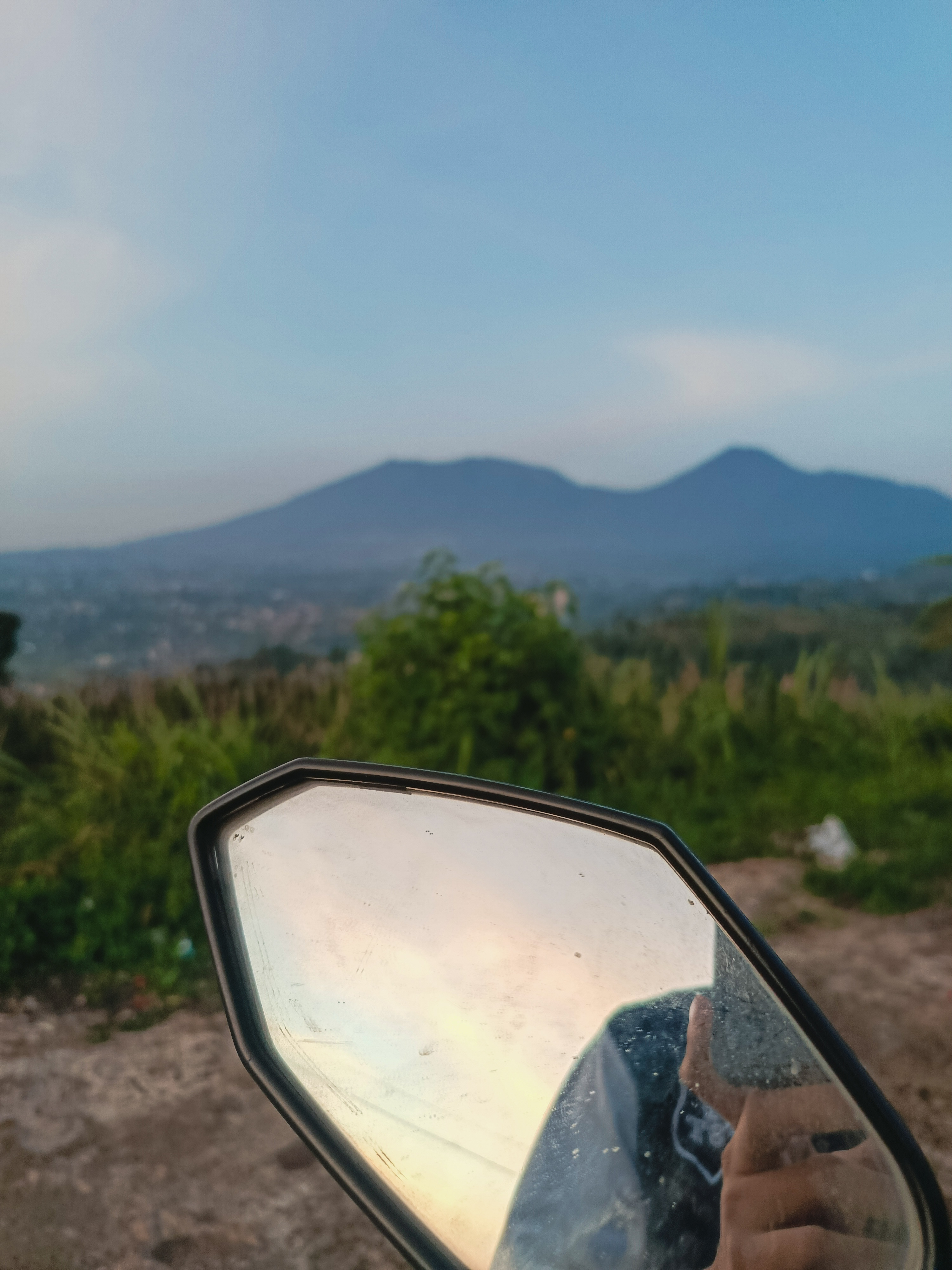 A motorcycle mirror reflection with mountain scenery in the morning